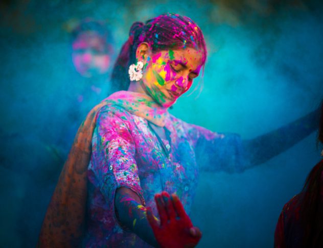 Young woman dancing around blue powder while celebrating the Indian Holi Day